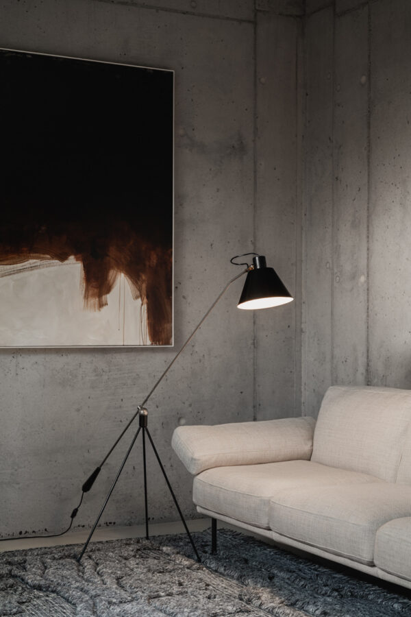 Zwarte Magneto vloerlamp (Matt Black van Atelier Artiforte ontworpen door Henk Willekes 1954 naast witte bank voor betonlook muur